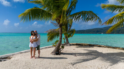 Romantic getaway from a married couple, The man and woman are hugging on a small tropical island with a sandy beach and tiny palm tree under blue sky. The people are surrounded by azure ocean sea 