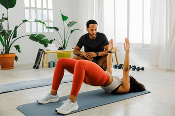 Personal trainer guiding woman doing bridge exercise at gym