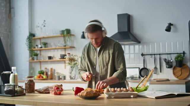 Singing man chopping pepper in kitchen apartment wearing earphones. Cheerful guy
