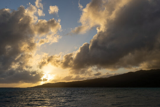 Sunrise behind tropical island Taha'a in French Polynesia. The paradise destination is surrounded by south pacific ocean sea water. 