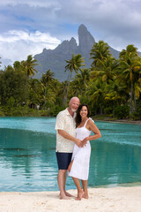 Happy, middle aged couple together on vacation on tropical island Bora Bora. Palm trees, an azure ocean lagoon and Mount Otemanu can be seen in the background. 
