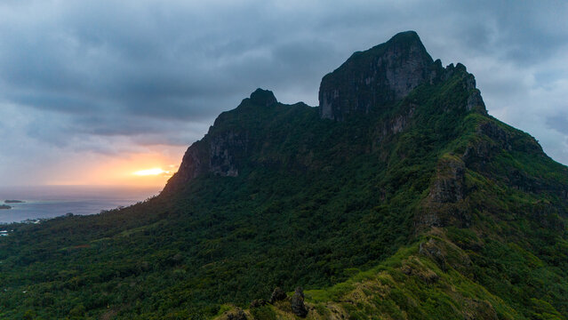 Sunset behind Mount Otemanu on the tropical island Bora Bora. The mountain is covered with low clouds in the sky. The view of ocean water is beautiful. 
