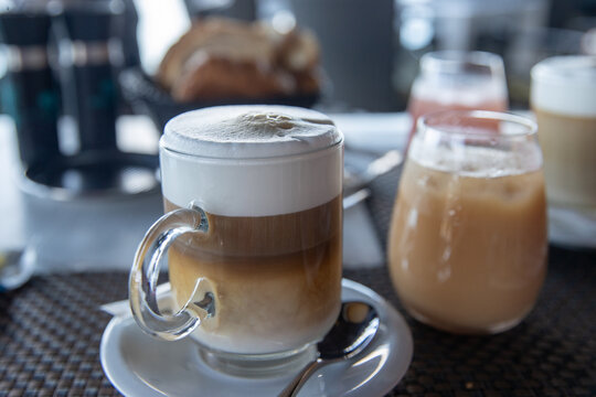 Fresh hot cappuccino coffee with a frothy top. The caffeine drink is served in a glass mug in a cafe or diner. Another popular option is a latte. 