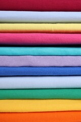 Stack of clean colorful t-shirts as background, closeup