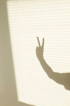 Golden hour minimal hand peace sign window shadow reflection on a wall
