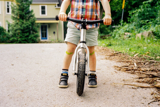 Anonymous Child with Band Aids on Each Knee Rides his Balance Bike