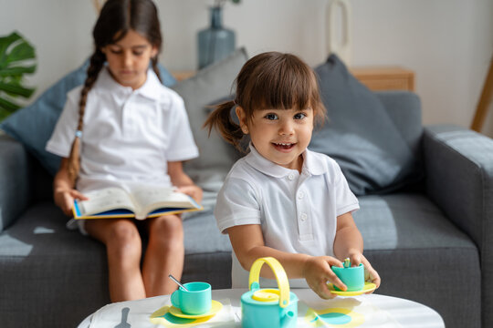 girl playing with tea set while sister is reading a book