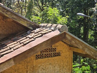 A close-up view of the roof of a traditional bamboo house, featuring a weathered clay tile roof and woven bamboo walls