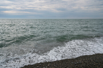 An incoming wave on the Black Sea and a pebble beach on the Sochi coast on a summer day with clouds, Sochi, Krasnodar Territory, Russia