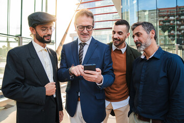 A group of businessmen watching their investments on a mobile phone. Corporate males browsing the internet on a smartphone. Office workers displaying his phone to his business partner at a startup
