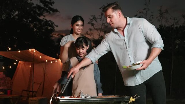Family together camp in garden, Mom dad and daughter grill food for family member. Outdoor camping activity to relax with nature and spend time with young generation cross generation gap. Divergence.
