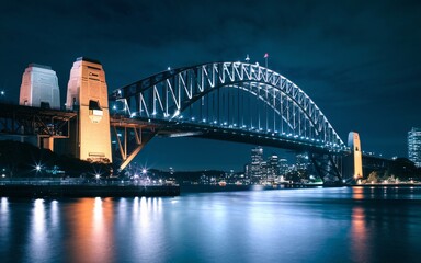 Fototapeta premium Harbour Bridge at Night: Illuminated Sydney Skyline with Reflections Background