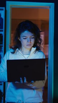Vertical video Computer scientist walking at home, developing software applications using laptop. IT professional standing in living room, implementing and maintaining company systems, camera B