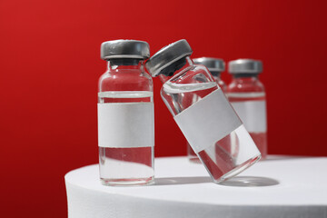 Glass medical bottles with vaccine on white table on red background, close up