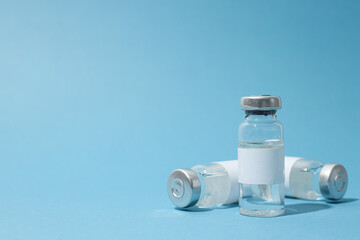 Glass medical bottles with vaccine on blue background, space for text