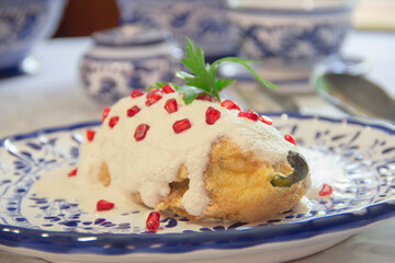 Chile en Nogada, roasted and stuffed poblano pepper with pecans white sauce and fresh pomegranate, served over talavera plate.