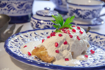 Authentic mexican Chiles en Nogada, roasted and stuffed poblano pepper with walnut white sauce and fresh pomegranate, served over talavera plate at Puebla city, Mexico.
