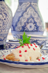 Chiles en Nogada, roasted and stuffed poblano pepper with walnut white sauce and fresh pomegranate, served over talavera a plate.