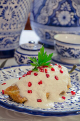 Chiles en Nogada, roasted and stuffed poblano pepper with walnut white sauce and fresh pomegranate, served over talavera a plate.