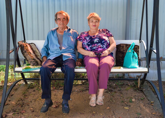 Old Russian married couple sitting on swings together