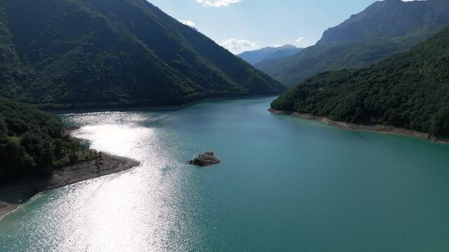 Flying low over the turquiose lake Pivsko near Pluzine surrounded by green forrests and mountains in Montenegro druing august summertime