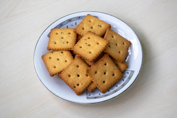 Delicious cracker biscuits on a white plate on a light wooden surface. Biscuits can be enjoyed anytime, including breakfast, lunch, dinner, or as a dessert. A tasty tea-time snack concept.