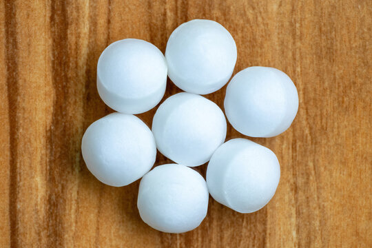 White Naphthalene balls isolated on wooden background. It is also known as mothballs, moth flakes, naphthalin, antimite, hexalene, tar camphor, and white tar. Top view.