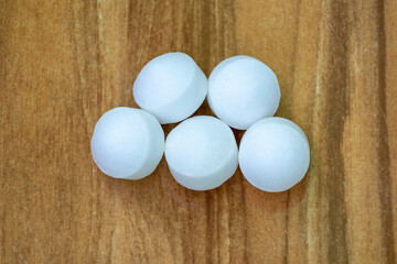 White Naphthalene mothballs isolated on wooden background. It is also known as moth flakes,...