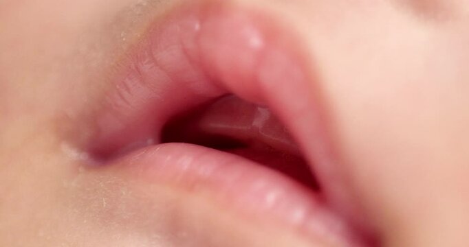 Blurry close-up shot of the opened mouth of a sleeping newborn baby showing her pinkish lips and smooth skin.