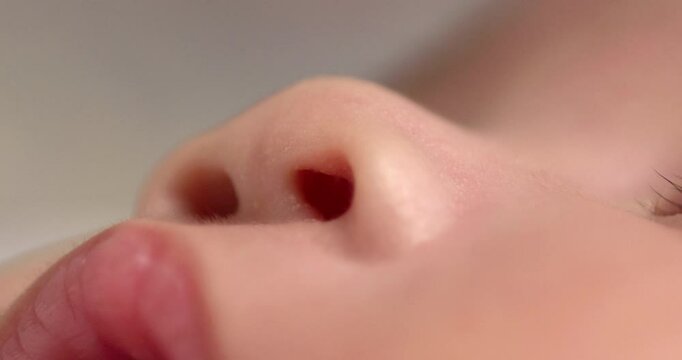 Close-up shot of the nostrils of a sleeping newborn child and showing her upper lip and some parts of her lashes.