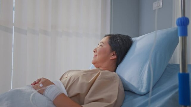 Asian mature female patient getting saline solution in hospital ward. 