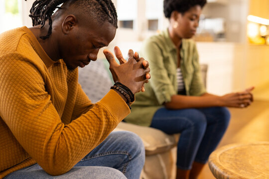 African American couple sitting on couch, deep in thought, facing away from each other