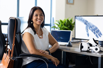 Smiling woman in office with laptop, VR headset, and robotic arm on screen