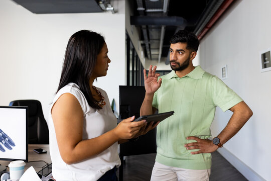 Discussing project, colleagues using tablet and gesturing in modern office setting