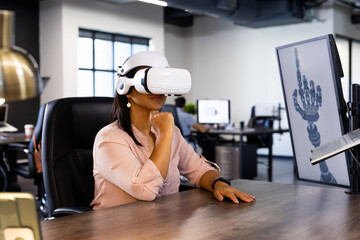 Using VR headset, woman exploring robotic hand design on computer in office