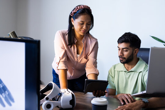 Using tablet and VR headset, colleagues discussing project in modern office workspace