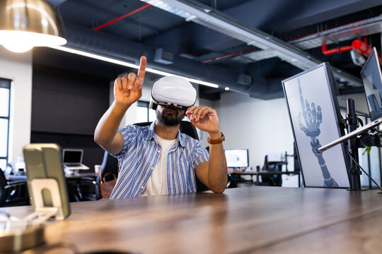 Using VR headset, Indian man interacting with virtual interface in modern office