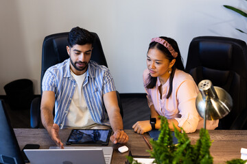 Discussing project, colleagues using laptop and tablet in modern office setting