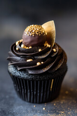 A luxurious black and gold-themed cupcake with dark chocolate frosting, gold leaf accents, and a chocolate truffle on top