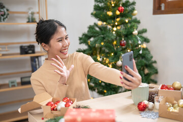 Happy young woman using smartphone mobile addict spending time in front of Christmas tree at home celebrating new year and Christmas