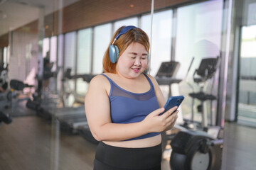 Fototapeta premium Obese asian woman Enjoy listening to music. Fat Female with headphones smart phone after workout at Gym