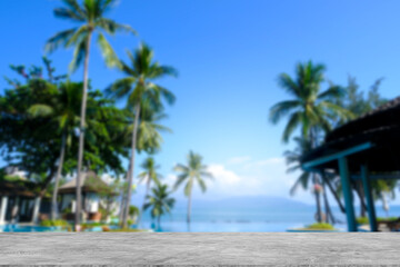 Fototapeta premium Cement counter top There is a view of the swimming pool and sea in the background of the resort. A blurry garden of trees is visible. of decorative design ideas