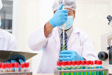 Two Asian scientists in lab coats sit at a table in a laboratory, examining samples through a...