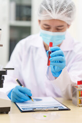 Two Asian scientists in lab coats sit at a table in a laboratory, examining samples through a...