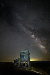 Long exposure milky way over an abandoned house in the desert with town lighting the background