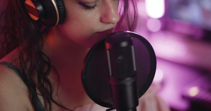 Female music producer in studio with audio recording equipment. Girl snging on a professional studio microphone. Close up abstract video.