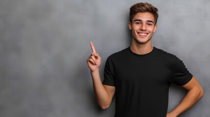 Young man isolated on gray textured wall, smiling while pointing with index finger to black t-shirt, copyspace for advertising