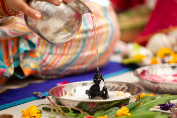 Indian woman performing snan ritual by pouring water on (Laddu Gopal) Hindu god Krishna, during the Indian festival of Krishna Janmashtami.