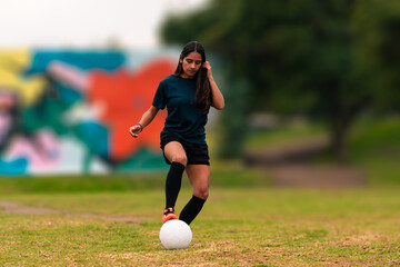 Beautiful brunette latina woman running, training and playing soccer on a green field, with colorful background, wearing sportswear, advertising and sports wellness.