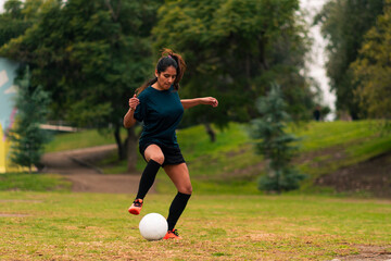 Beautiful brunette latina woman running, training and playing soccer on a green field, wearing sportswear, advertising and sports wellness.